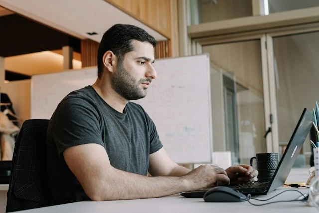 A professional sitting at a desk in an office environment and typing on a laptop.